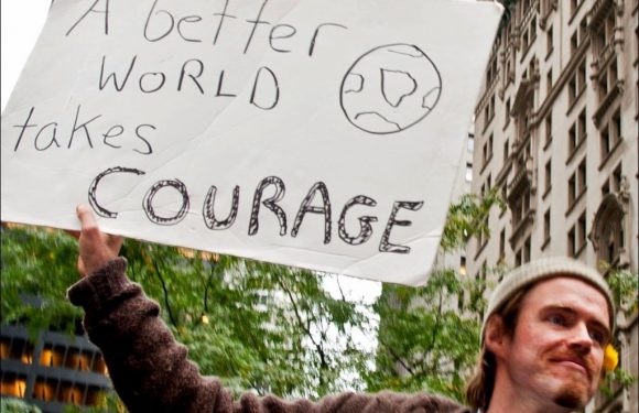 Man with sign "A Better World takes Courage"