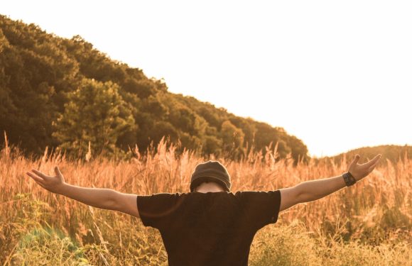 Man sitting in a field with his arms open wide