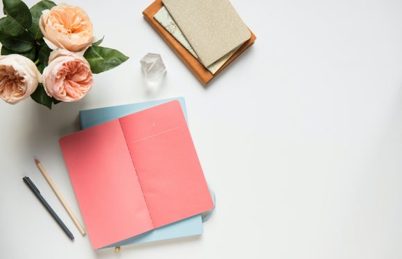 Flat lay of cards, pens, and small vase of peach colored flowers