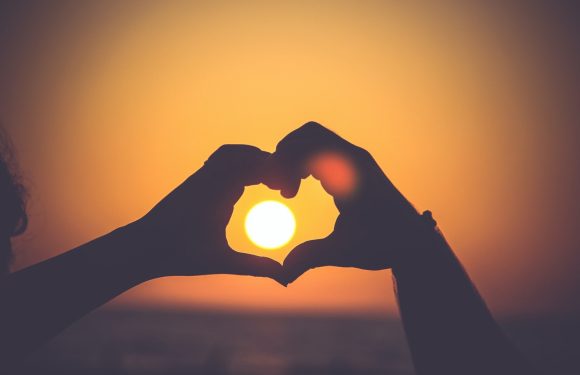 Hands in the shape of a heart with sun in the background