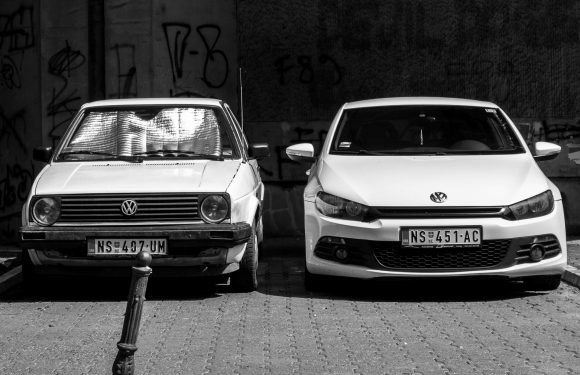 2 Volkswagon cars, both white.  One old and one new.