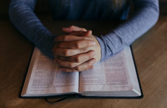 Man praying while laying his hands on the bible