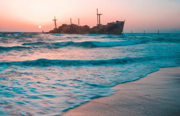 Ocean beach at sunset with wooden ship in background