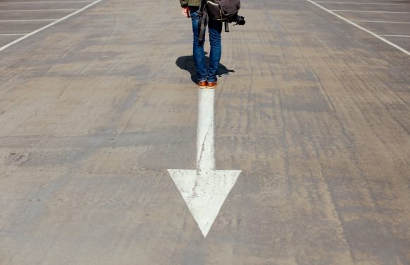 Traveler standing backwards on an arrow pointed in the opposite direction of a path.