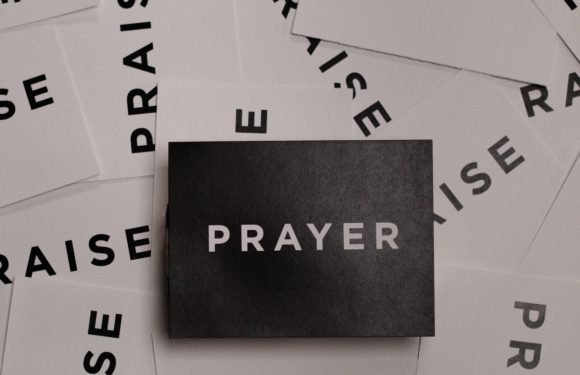 Black post card with the word Prayer in white centered on top of white post cards with the word praise scattered underneath