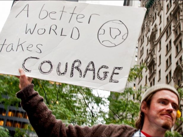 Man with sign "A Better World takes Courage"