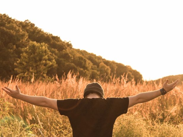 Man sitting in a field with his arms open wide