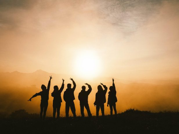 6 people silhouetted in front of a hazy golden sky