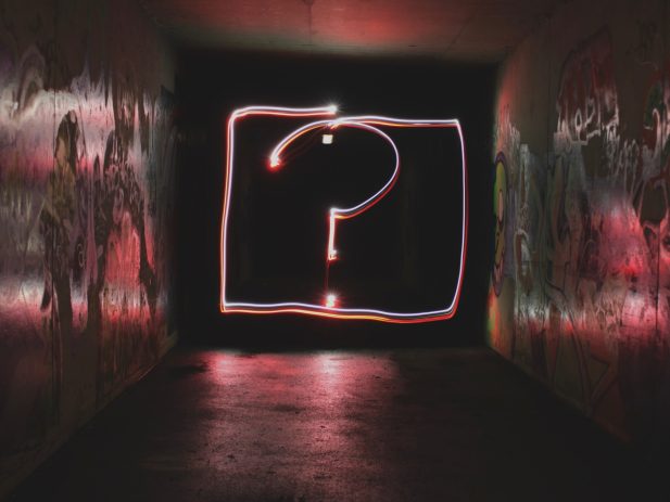 Dark hallway with graffiti on the walls, question mark created by glow lights at the end of the hallway