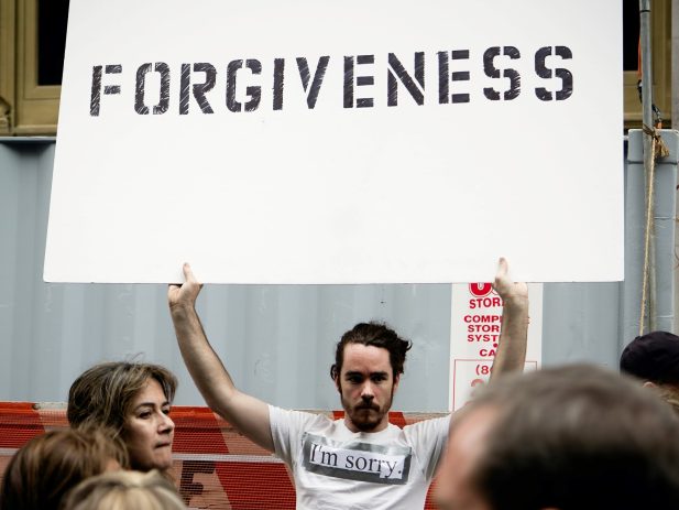 Man holding a "Forgiveness" sign and wearing a "I'm Sorry" t-shirt