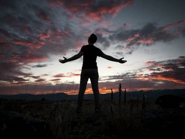 Silhouette of person with outstretched arms in front of sunset landscape