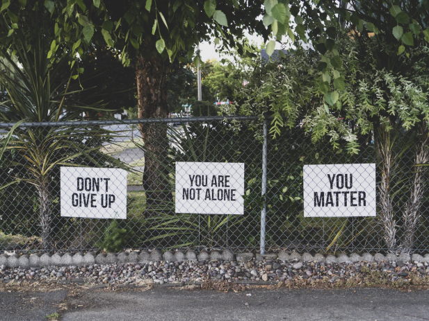 Chainlink fence with encouraging posters saying "Don't Give Up, You Matter, You are not alone" in front of trees