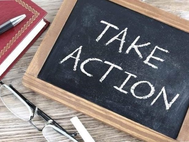 Chalkboard with words "Take action" next to reading glasses, a pen and a notebook.