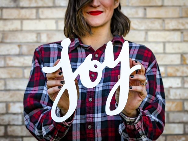 Woman in plaid shirt holding sign that says "Joy"