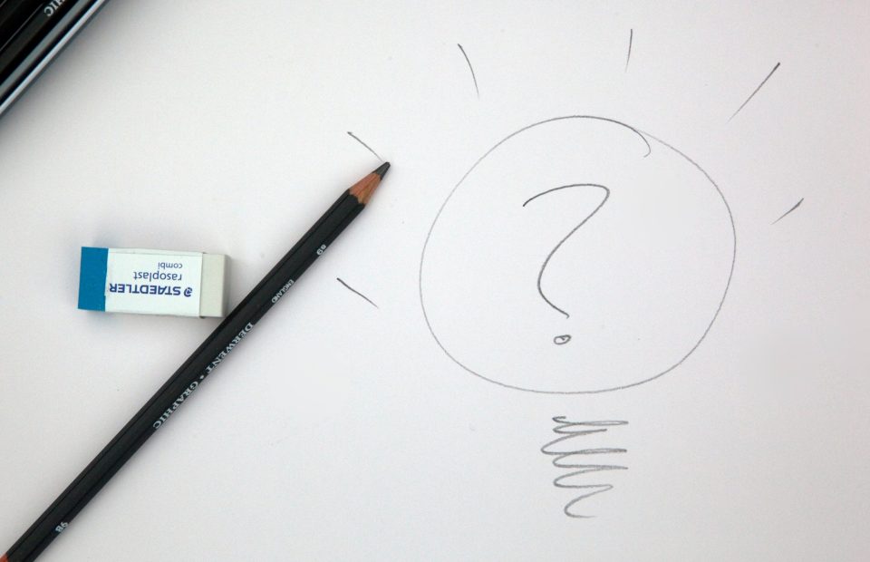 Large circled question mark drawn on a piece of white paper with a black colored pencil and a white eraser lying on the left side