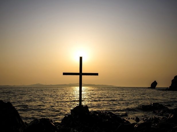 Cross near the sea with sun behind